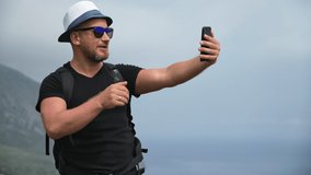 Smiling male travel blogger backpacker shooting video online live air broadcasting on top of high mountain. Happy man trendy vlogger talking internet call use smartphone on cliff over sea landscape