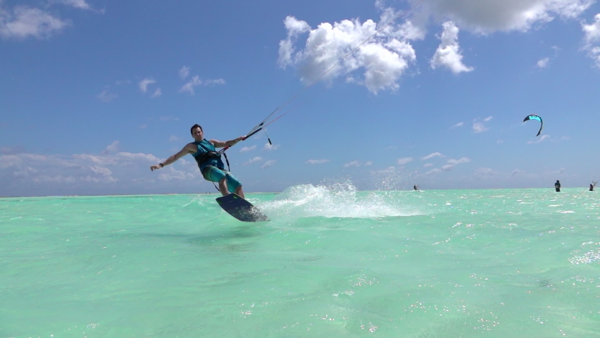 SLOW MOTION, CLOSE UP: Young kiteboarder surfing in Zanzibar jumps and does a spin trick while riding around the turquoise lagoon. Kitesurfer splashes glassy ocean water while riding in Zanzibar. Royalty-Free Stock Footage #1075161689