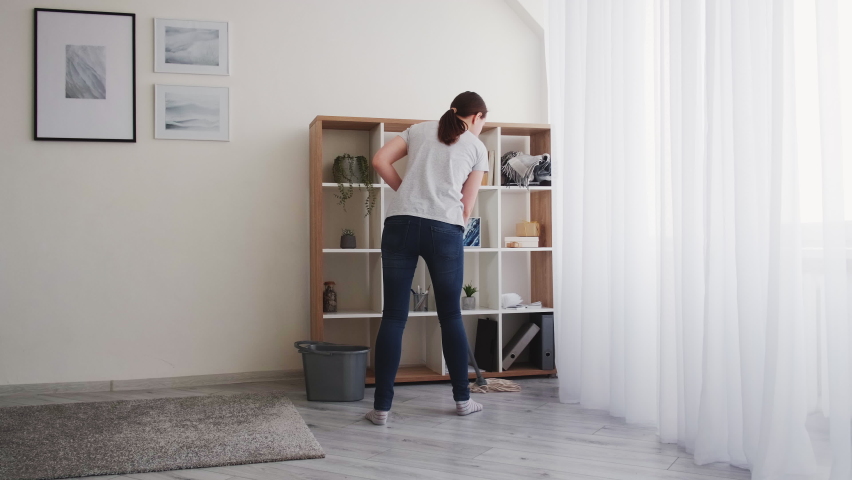 Home cleaning. Housework routine. Room hygiene. Housekeeping procedure. Woman in jeans and t-shirt washing laminated floor with mop.
