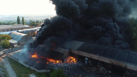 Heavy smoke in a burning industrial distribution warehouse or warehouse industrial hangar. View from a drone that shoots a large-scale fire. Black smoke from the fire still continues from the factory