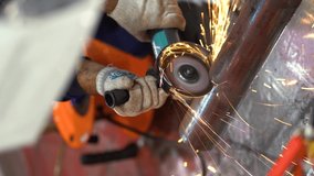 One unrecognizable worker man wear protective gloves, blue jacket uses grinder, saws and turns metal pipe with large diameter into parts at factory background close up view. Sparks fly around guy. 
