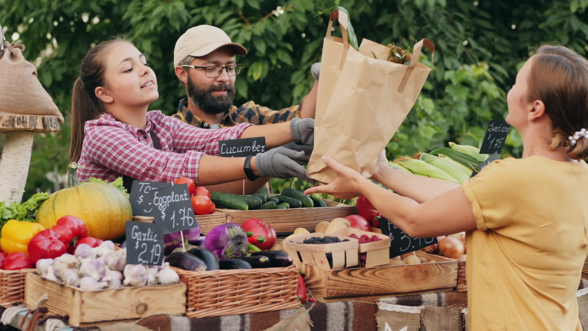 Happy smiling farmers father and his teenage daughter handing eco paper bag with fresh vegetables to woman buyer at farmer's market Royalty-Free Stock Footage #1075174484