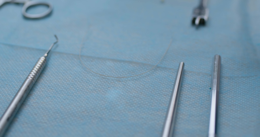 A close-up metal archwire is laying on the table and a medical worker is taking the wire than by using orthodontic wire cutters straight is bite off a piece of wire. Royalty-Free Stock Footage #1075178633
