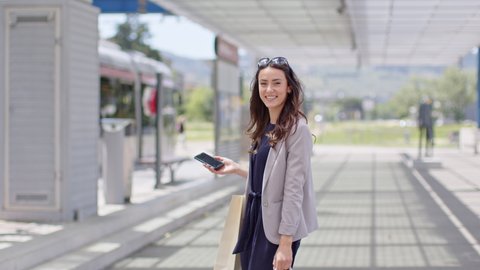 Woman standing at train station with shopping bags and smartphone