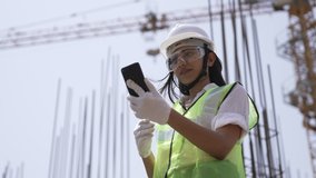 Indian engineer holding smartphone and making video call with costumer about building information,Asian female standing in work site,he feeling happy and smiling,video call and internet technology.