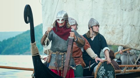 Vikings Sail on an Ancient Ship Along the River Against the Backdrop of the Rocky Coast. Men in Armor in Helmets with a Sword are Preparing to Attack. Medieval Reconstruction. Stock Video