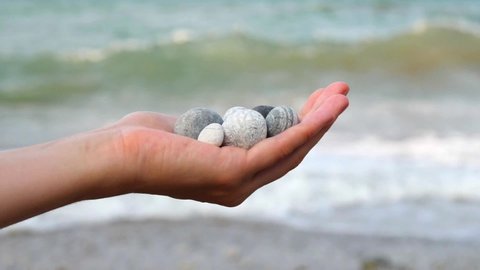 Blurry defocus Beautiful round gray and white sea stones lie in a female hand against background of sea and waves. The concept of relaxation, vacation and meditation, zen, Cyprus. Slow motion video.
