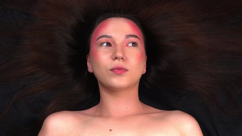 Beautiful young model posing for a photographer. Fashionable model with bright makeup on a black fabric background. 4k footage