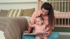 Childcare at Home, Child Protection, New Life, Leisure with Baby. Mom reads a book to the kid while sitting near the bed at home - Powered by Shutterstock - Get 15% off with code: PIKWIZARD15