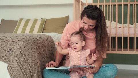 Childcare at Home, Child Protection, New Life, Leisure with Baby. Mom reads a book to the kid while sitting near the bed at home