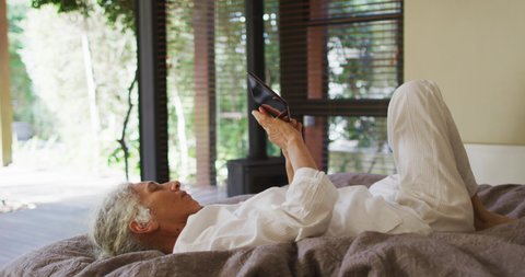 Senior mixed race woman lying in bed using tablet. retirement and senior lifestyle, spending time alone at home.