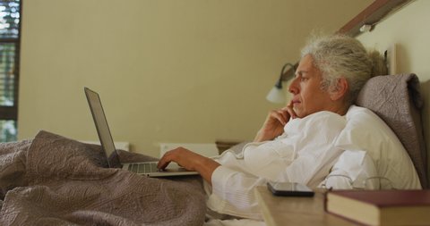Senior mixed race woman lying in bed using laptop. retirement and senior lifestyle, spending time alone at home.