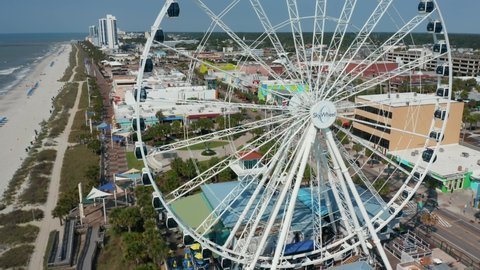 Myrtle Beach , SC , United States - 06 15 2021: SkyWheel ferris wheel. Aerial pullback reveals boardwalk promenade at family vacation beach destination in America.
