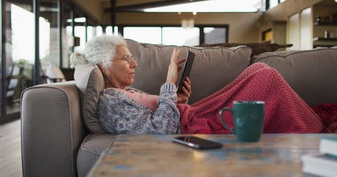 Senior mixed race woman lying on sofa using tablet. retirement and senior lifestyle, spending time alone at home.