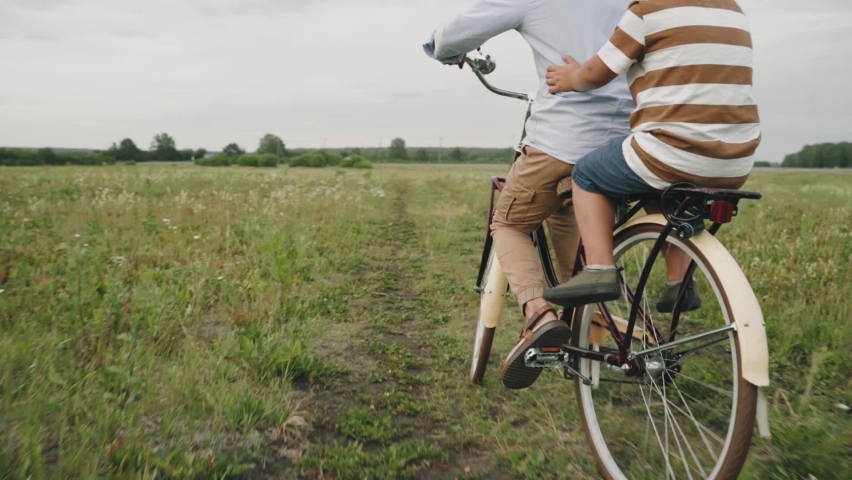 A man carries a child on a retro bike. Father and son are driving through a flower field. Retro style. A fashionable bicycle. Self-isolation. Outdoor recreation. Country life Slow motion