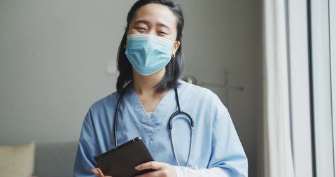 Portrait of happy asian female nurse wearing face mask holding tablet in hospital, smiling to camera. medicine, health and healthcare services during coronavirus covid 19 pandemic.