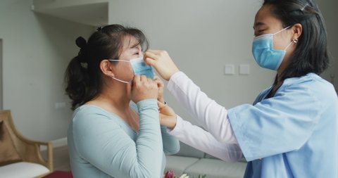 Asian female nurse and patient wearing face masks talking and looking to camera in hospital. medicine, health and healthcare services during coronavirus covid 19 pandemic.