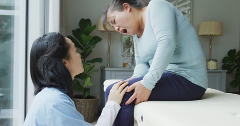 Asian female physiotherapist examining female patient holding knee in pain at surgery. physiotherapy, health and healthcare services.