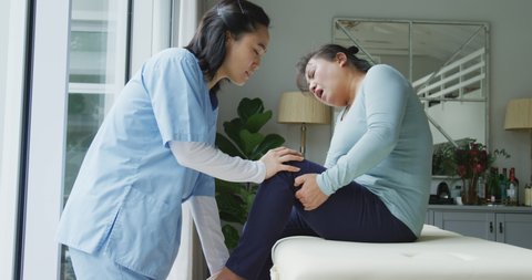 Asian female physiotherapist treating female patient holding knee in pain at surgery. physiotherapy, health and healthcare services.