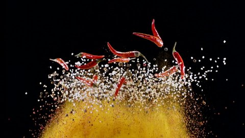 Mixture of ground spices, assorted peppers, salt and small red chili peppers slowly rise and fall against a black background. 300fps
