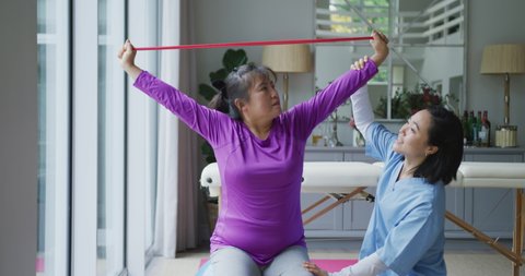 Asian female physiotherapist helping female patient exercise arms with exercise band at surgery. physiotherapy, health and healthcare services.