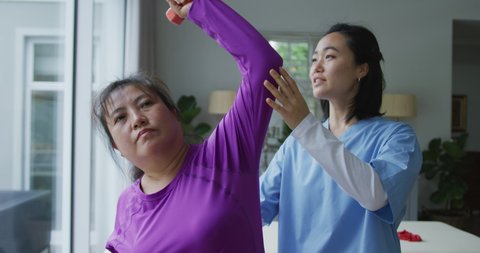 Asian female physiotherapist helping female patient exercise arms with dumbbells at surgery. physiotherapy, health and healthcare services.