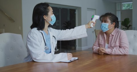 Asian female nurse wearing face mask taking temperature of female patient wearing mask in hospital. medicine, health and healthcare services during coronavirus covid 19 pandemic.