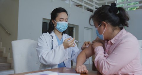 Asian female nurse wearing face mask giving covid vaccination to female patient in hospital. medicine, health and healthcare services during coronavirus covid 19 pandemic.