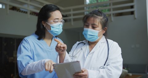 Portrait of asian female doctors wearing face masks, using tablet and discussing in hospital. medicine, health and healthcare services during coronavirus covid 19 pandemic.