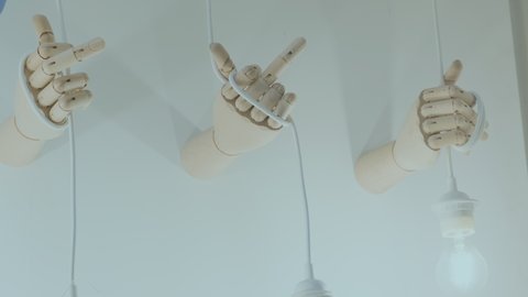 Three wooden arms on wall with glowing light bulbs hanging. Hands show an indecent gesture with middle finger. Concept of switching off the light and electricity, modern art, art house