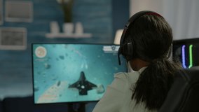 Closeup of competitive black woman player holding joystick playing space shooter video game at powerful computer late night. Professional gamer using wireless controller for online gaming championship