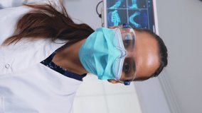 Vertical video: Patient pov to doctor in stomatological office treating teeth of woman. Orthodontic specialist and man assistant working wearing masks and gloves in modern dental clinic.