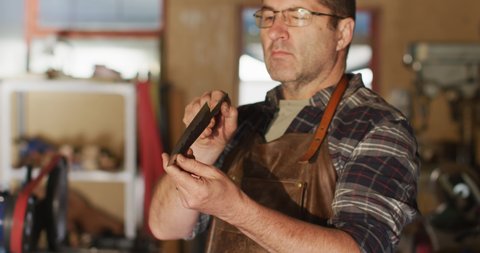 Midsection of caucasian male knife maker in workshop, holding knife. independent small business craftsman at work.