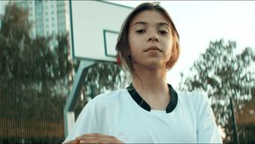 Portrait of Caucasian teenager girl basketball player posing outdoor on a streetball court, looking into camera. Shot with 2x anamorphic lens - Powered by Shutterstock - Get 15% off with code: PIKWIZARD15
