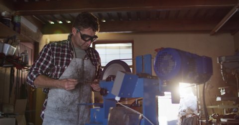 Caucasian male knife maker in workshop wearing glasses and using saw. independent small business craftsman at work.