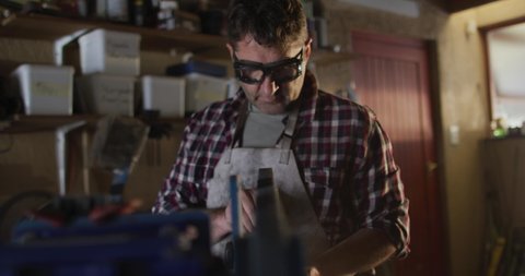 Caucasian male knife maker in workshop wearing glasses and using sander. independent small business craftsman at work.