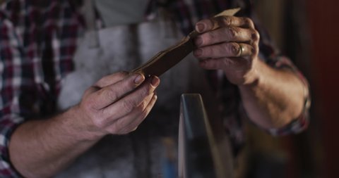 Close up of caucasian male knife maker in workshop wearing glasses and using sander. independent small business craftsman at work.