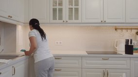 Housewife doing household chores, woman cleaning kitchen, modern white apartment interior with open floor plan. High quality 4k footage