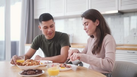 The smiling woman feeding man breakfast with fork while sitting in the kitchen