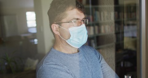 Caucasian man wearing face mask, looking through window. staying at home during coronavirus covid 19 pandemic.
