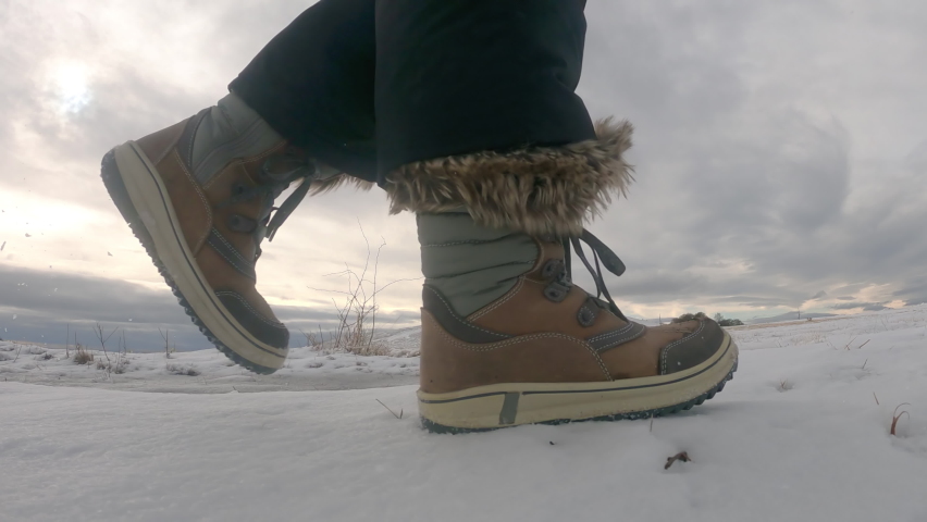 Close u of womans boots walking on the snowy mountain road in the winter day