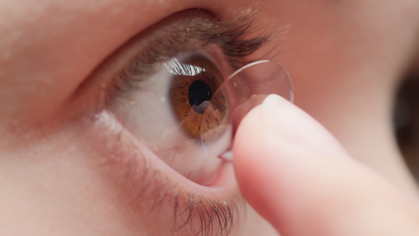 Close-up of a brown-eyed young woman putting on the contact lens with fingers and blinking. Advertising of contact lenses for vision improvement. Optical shop, health care and medicine concept. Royalty-Free Stock Footage #1075242056