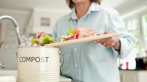 Close Up Of Woman In Kitchen Making Compost Scraping Vegetable Leftovers Into Bin