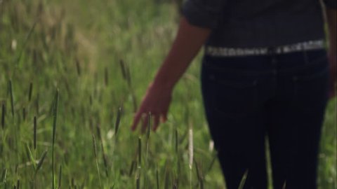Slow motion of a woman with a studded belt walking through tall green grass. Filmed with a high speed camera.