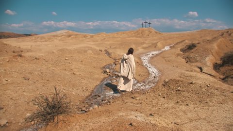 Christ walks through the desert. In the background you can see three crosses. The Holy Road to Golgotha - metaphorical concept