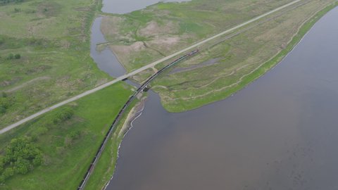 A drone view of a freight train driven by a diesel locomotive on a single-track railroad among green fields, small rivers and wetlands