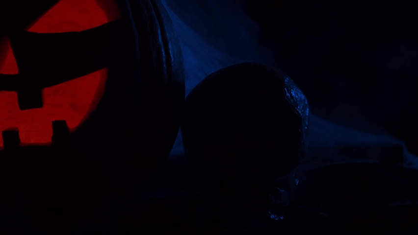 Scary laughing pumpkin and an old skull on a dark background. Halloween, witchcraft and magic.