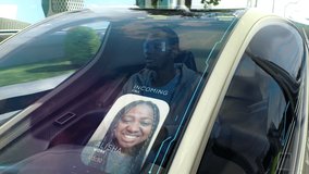 Zoom out view of African American guy riding futuristic anti gravity vehicle and speaking with girlfriend via windshield interface in city