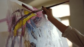 Talented woman hand making yellow brush stroke on canvas in art studio. Unrecognizable painter painting abstract picture indoors. Unknown female artist holding paintbrush at art workplace.