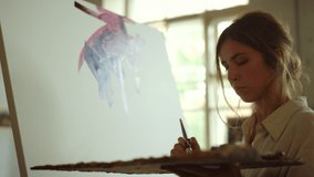 Young woman painting modern picture indoors. Creative girl applying paint on canvas in art studio. Beautiful female painter drawing abstract artwork with oil paint at art workplace.